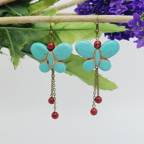 Handmade turquoise butterfly dangle earrings with red bead accents and antique brass chain drops – boho insect-inspired jewelry for women